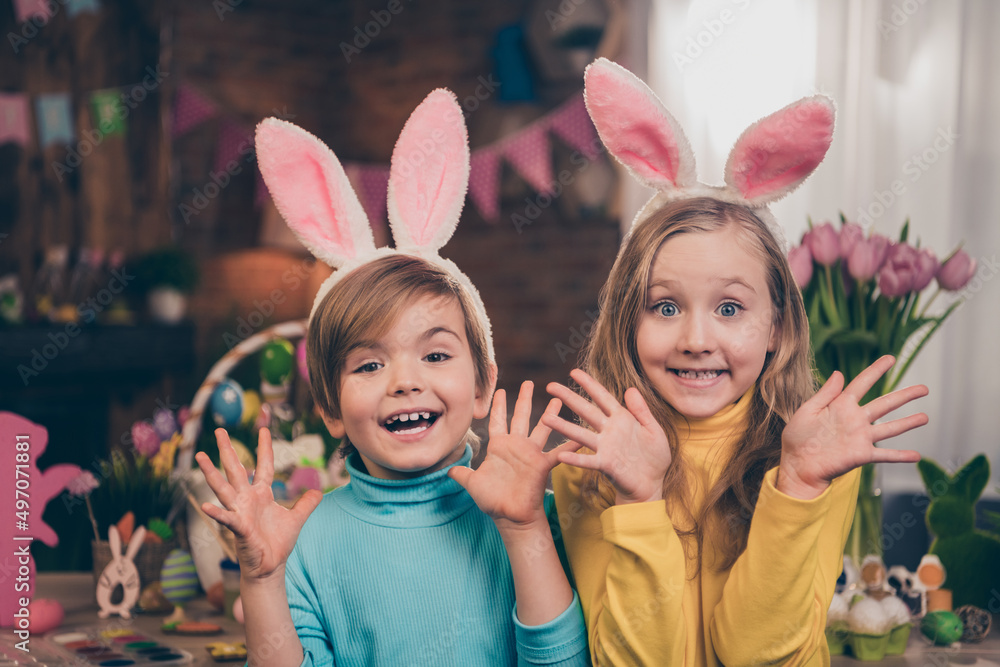 Portrait of two overjoyed carefree kids raise arms palms have fun beaming smile house indoors Portrait of two overjoyed carefree kids raise arms palms have fun beaming smile house indoors