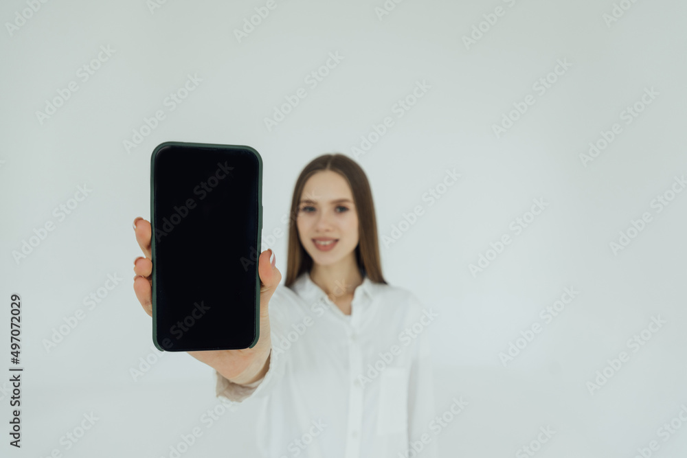 Portrait of an excited young business woman pointing finger at blank screen mobile phone over white background Portrait of an excited young business woman pointing finger at blank screen mobile phone over white background