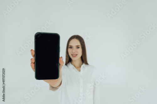 Portrait of an excited young business woman pointing finger at blank screen mobile phone over white background