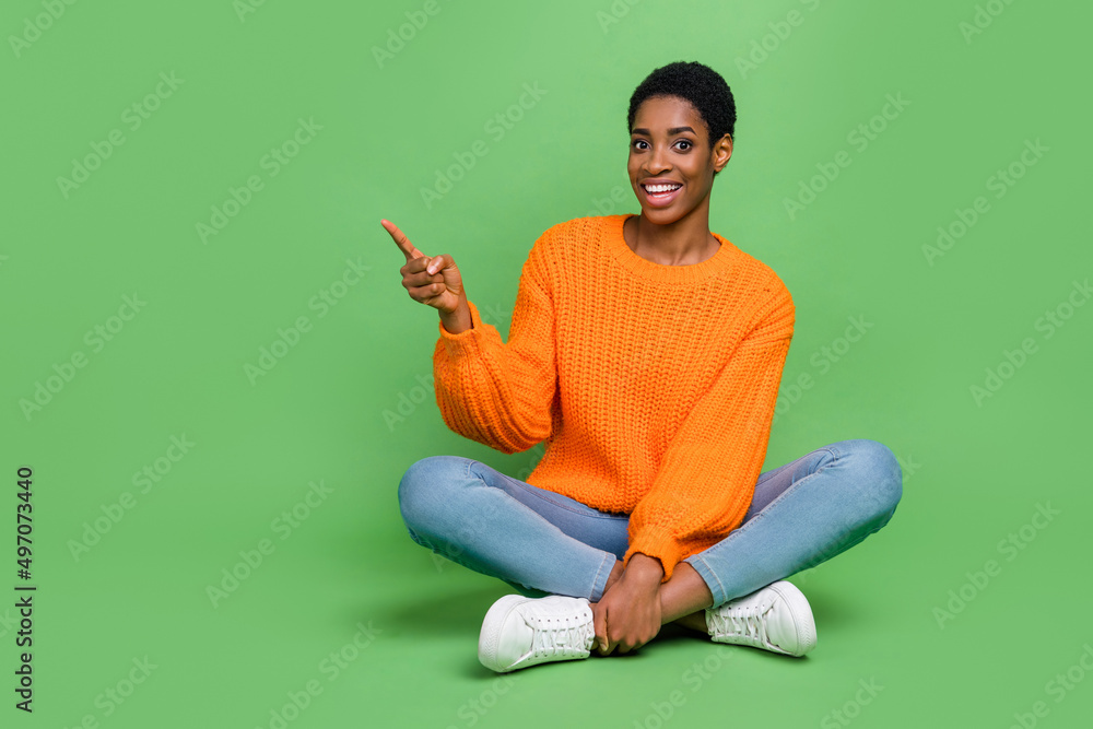 Full body photo of sweet young short hairdo lady sit index promo wear sweater jeans shoes isolated on green color background Full body photo of sweet young short hairdo lady sit index promo wear sweater jeans shoes isolated on green color background