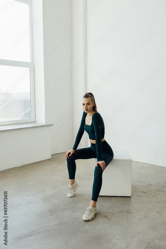 Fit young woman sitting on a box after exercising. Woman wearing sports clothing looking at camera Fit young woman sitting on a box after exercising. Woman wearing sports clothing looking at camera