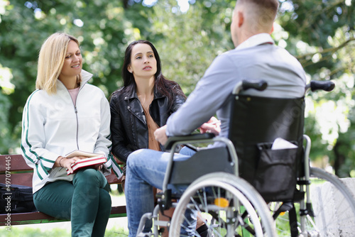 Two women communicate with man in park in wheelchair