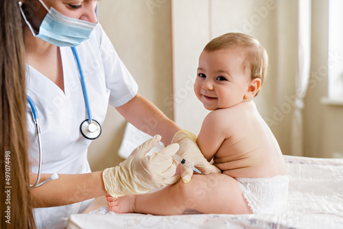 Fototapete Young female pediatrician or nurse giving an intramuscular injection of a vaccine to leg of little baby boy Immunization for children concept