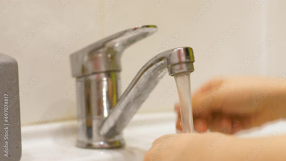 Close-up of a child opens the faucet turns on the water and washes his hands over the sink in the bathroom. Washing children's hands concept. Hygiene and washing hands at home. Selective focus Close-up of a child opens the faucet turns on the water and washes his hands over the sink in the bathroom. Washing children's hands concept. Hygiene and washing hands at home. Selective focus