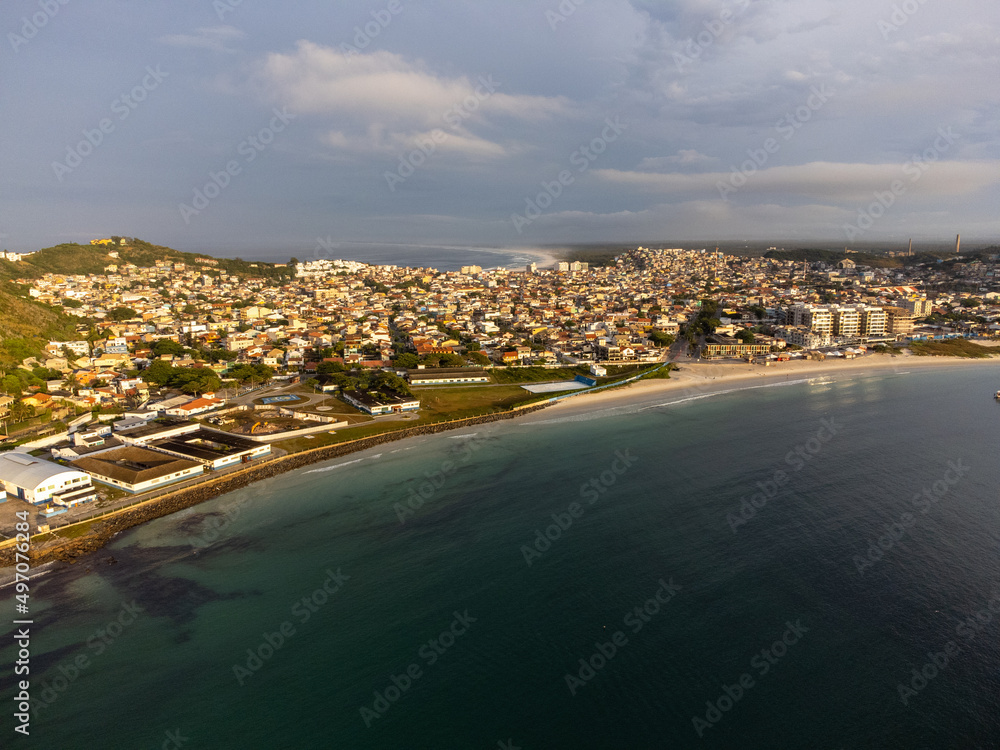Fototapeta premium Amazing sunset on a paradise beach with mountains, nature and city. Drone aerial view. Arraial do Cabo, Rio de Janeiro, Brazil