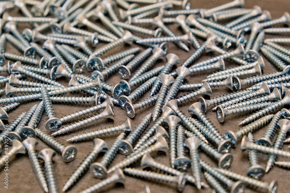 A lot of silver metal screws on the table close-up, background. Selective focus. A lot of silver metal screws on the table close-up, background. Selective focus.