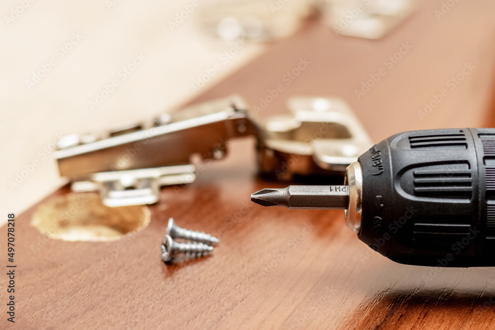 Cordless screwdriver near the cabinet door to which the hinges are attached