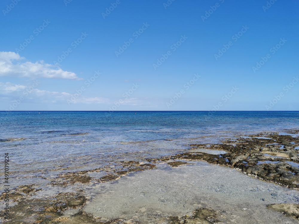  The coast of the Mediterranean Sea, long frozen lava, in the recesses of which there is sea water against a blue sky .