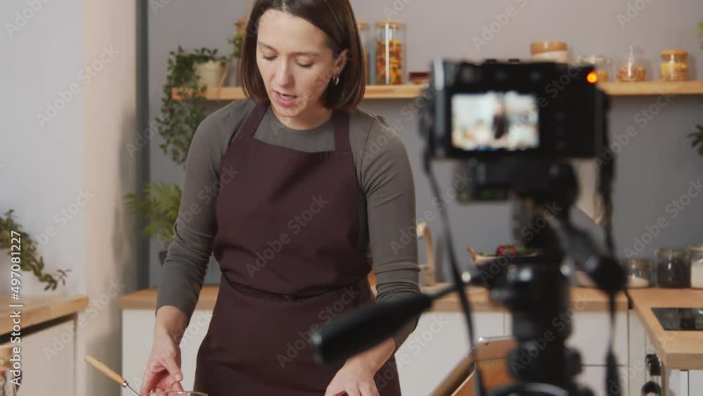 Selective focus shot of female culinary blogger showing food ingredients while filming video recipe in kitchen Selective focus shot of female culinary blogger showing food ingredients while filming video recipe in kitchen