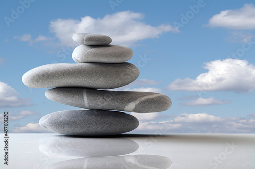 five grey stones balanced on white surface over blue sky