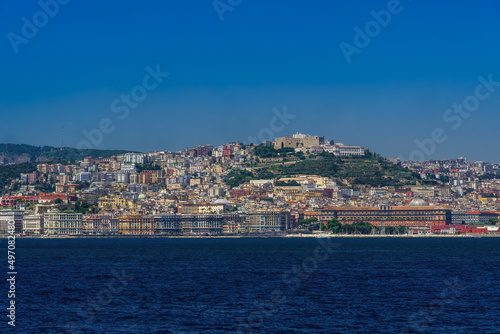 Naples  Italy city center coastal sea view under cloudless blue sky with Castel Sant Elmo medieval fortress and waterfront buildings visible from a sailing ship on the gulf.