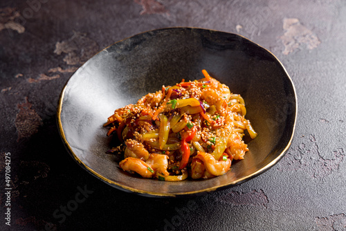 wok with shrimp and vegetables on black bowl on dark stone table