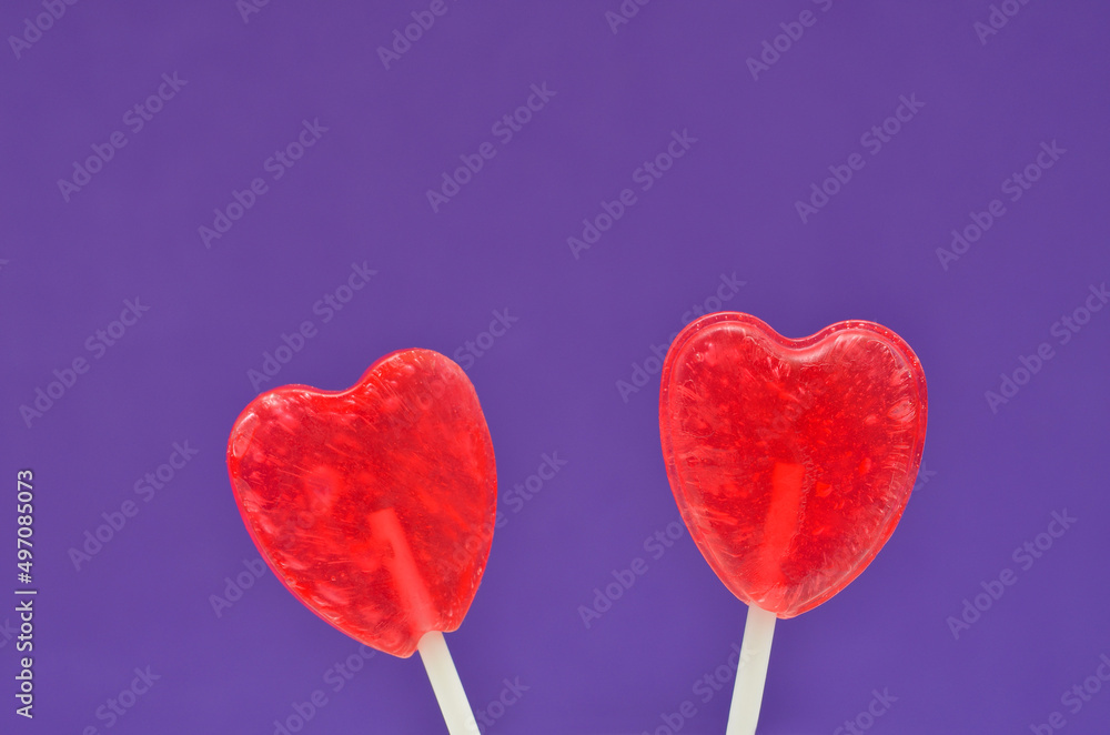 two heart-shaped lollipops on a lilac background