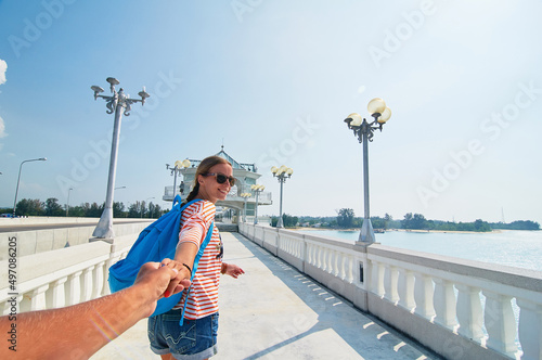 Follow me. Travel concept. Vacation on Phuket island. Back view of young woman holding boyfriend's hand enjoying sea view from bridge terrace.