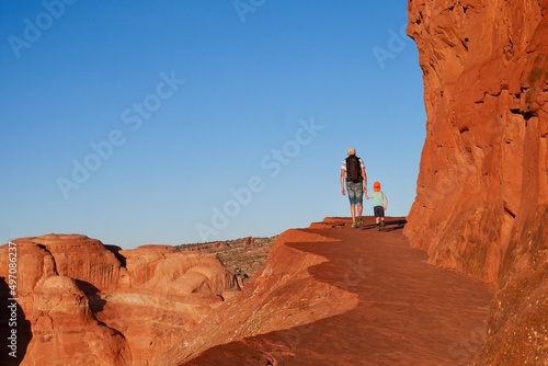 Father and son hiking on Delicate Arch trail at sunset. Family on summer vacation trip. Arches National Park, Moab, Utah, USA.
