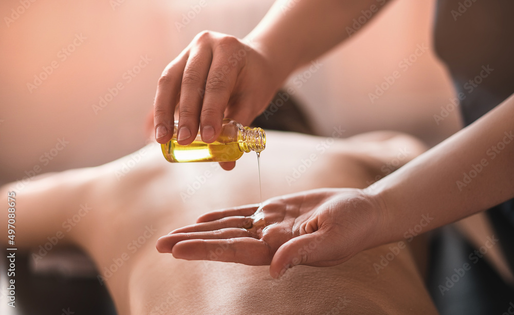 The masseur pours massage oil on his hand against the background of the back, a woman lying in the background in the spa. The concept of skin care in a beauty salon - obrazy, fototapety, plakaty 