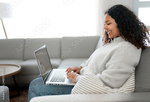 Attractive young African woman working on laptop while sitting on the couch at home