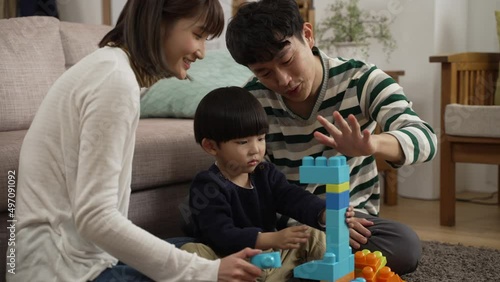 happy japanese family of three enjoying playing plastic building blocks in the living room at home. the father is helping hold the unstable bricks for his son to prevent them fall