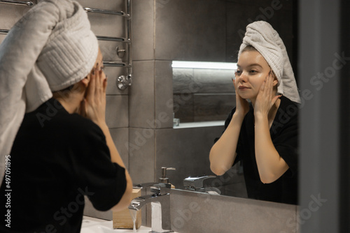 woman with a towel on her head washes her face with water in the bathroom