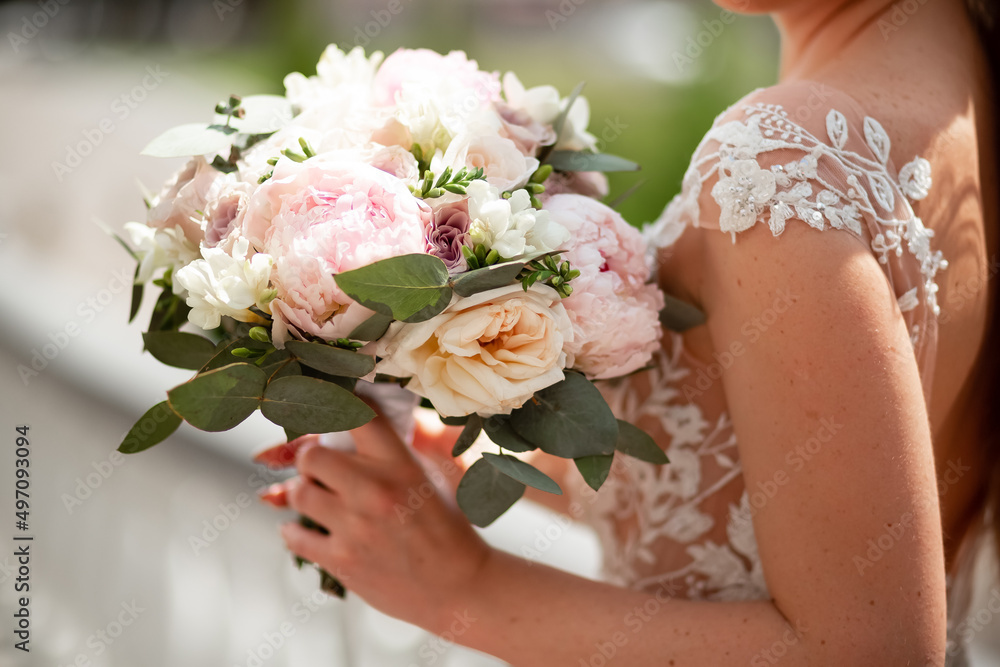 A beautiful bride holds a bouquet of roses in her hands and waits for her groom. Wedding traditions. Good weather in summer, when all around are bright and green leaves