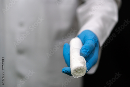 A young traumatologist holds a white medical bandage in his hand. A doctor in a white coat and a bandage in his hands on a black background.