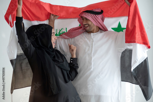 Happy Arab man and woman holding Irag flag, woman wears black Hijab Muslim traditional clothes, celebration concept photo