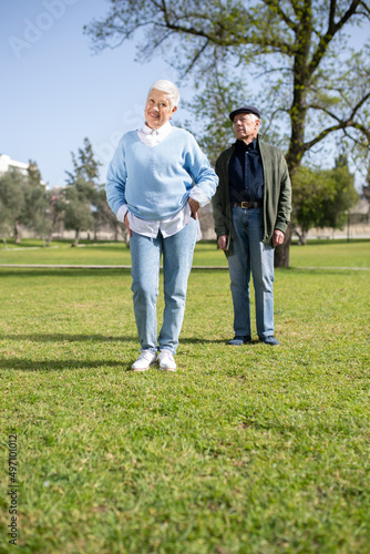 Portrait of modern aged couple posing on field. Attractive woman and man in casual clothes resting in park standing on grass looking aside. Relations and healthy lifestyle of aged people concept