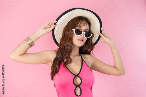 Happy attractive young beautiful woman in swimming suit wearing sunglasses and hat. Fashion portrait photo of elegant pretty girl isolated on pink background. Summer and beauty concept.