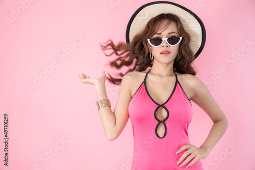Happy attractive young beautiful woman in swimming suit wearing sunglasses and hat. Fashion portrait photo of elegant pretty girl isolated on pink background. Summer and beauty concept.