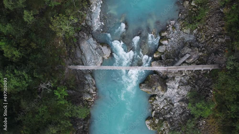 Aerial drone zoom in shot of aesthetic suspension old wooden bridge over epic mountain rocks and waterfall river. Scandinavian or northern hiking culture. Healthy adventure in outdoors