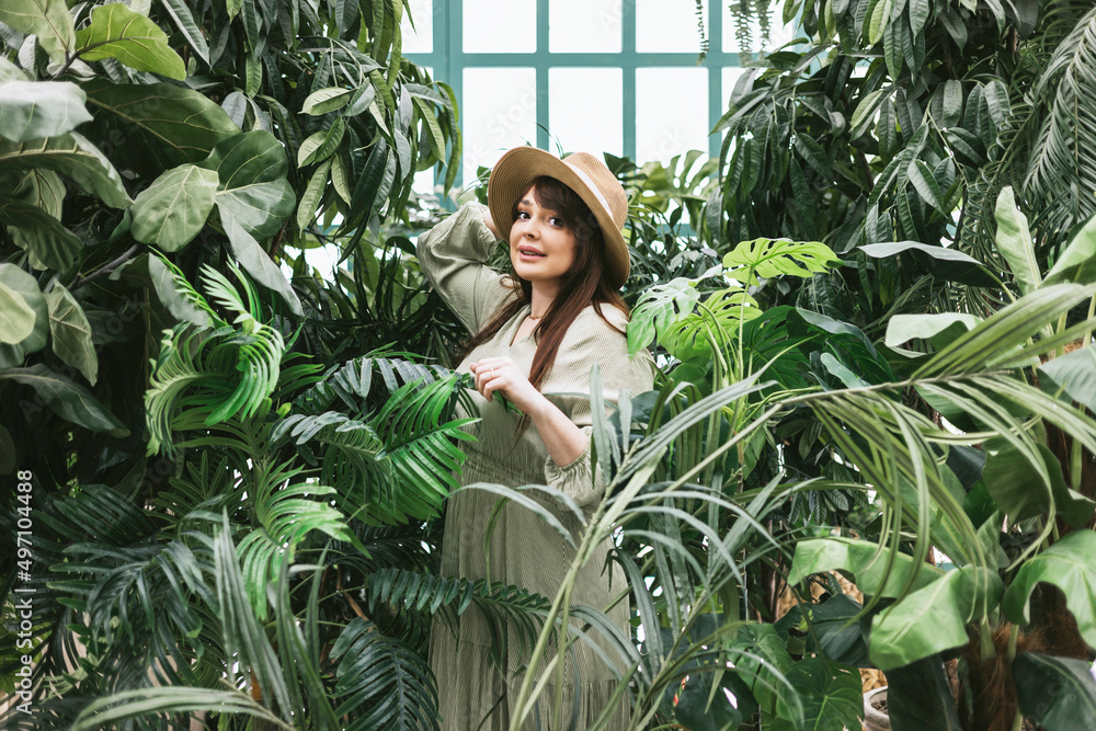 young woman plus size model in long green summer dress in greenhouse with tropical plants and potted plants, spring concept of urban and home jungles, place for rest and relaxation for mental health young woman plus size model in long green summer dress in greenhouse with tropical plants and potted plants, spring concept of urban and home jungles, place for rest and relaxation for mental health
