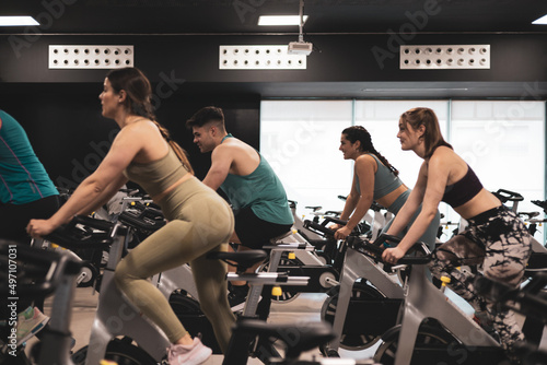 people on bikes in spinning class in modern gym, exercising on stationary bike. group of athletes training on exercise bike photo