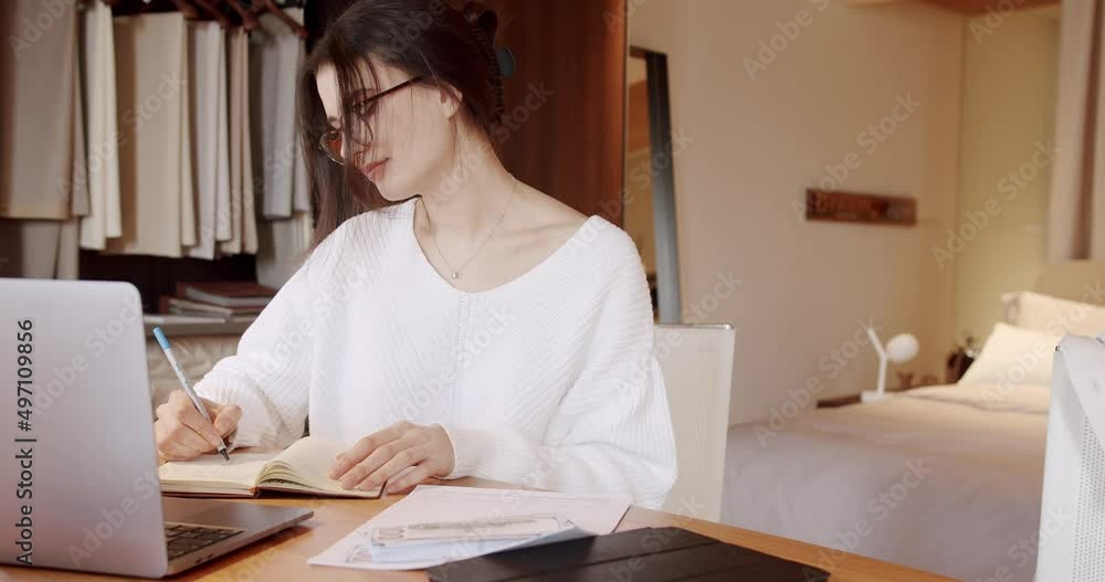 Millennial woman wearing headset making video chat working from home using laptop and make notes in your notebook. Reading data on the netbook and taking notes while working on the project at home. Millennial woman wearing headset making video chat working from home using laptop and make notes in your notebook. Reading data on the netbook and taking notes while working on the project at home.