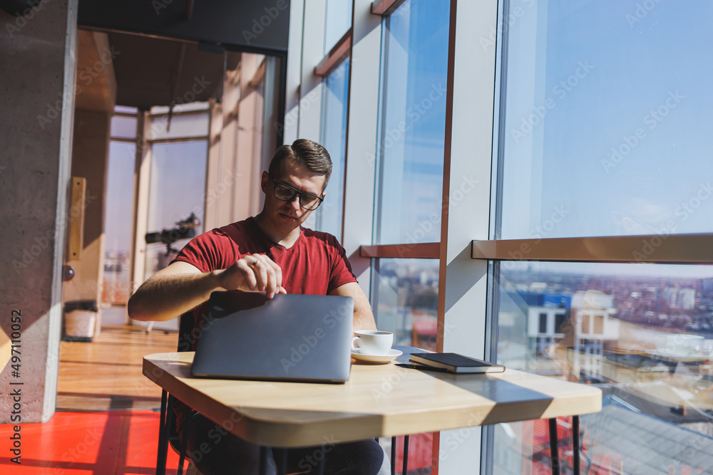 Portrait of a man, IT professional, working remotely with a modern laptop, sitting at a table and smiling at the camera during a break, a happy human programmer in vision correction glasses