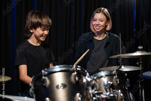 Young woman teaching boy to play drums.
