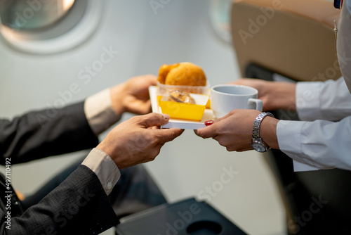 Close-up hands of passenger receive dessert and cake from air hostess or cabin crew during fly with airplane to other country.