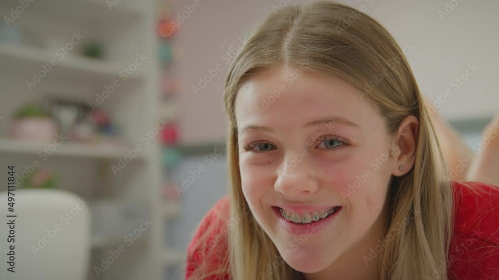Teenage girl wearing orthodontic braces lying on bed at home turns to face camera and smiles - shot in slow motion Teenage girl wearing orthodontic braces lying on bed at home turns to face camera and smiles - shot in slow motion