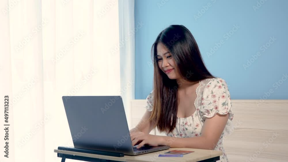 4K 50fps,Beautiful Asian girl, wearing a floral shirt, is ordering online on a laptop computer, happily, holding a credit card in her hand, picking up to pay with a credit card,online shopping. 4K 50fps,Beautiful Asian girl, wearing a floral shirt, is ordering online on a laptop computer, happily, holding a credit card in her hand, picking up to pay with a credit card,online shopping.