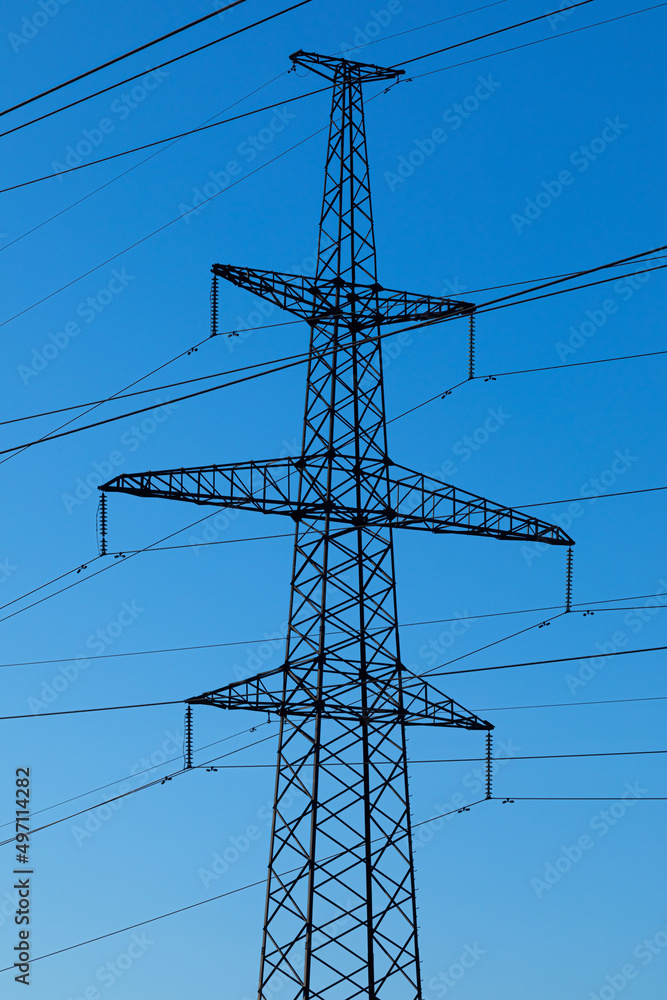 Background, view or scene of steel tower of electric main or electricity transmission line with the wires silhouette on background of clear blue sky Background, view or scene of steel tower of electric main or electricity transmission line with the wires silhouette on background of clear blue sky