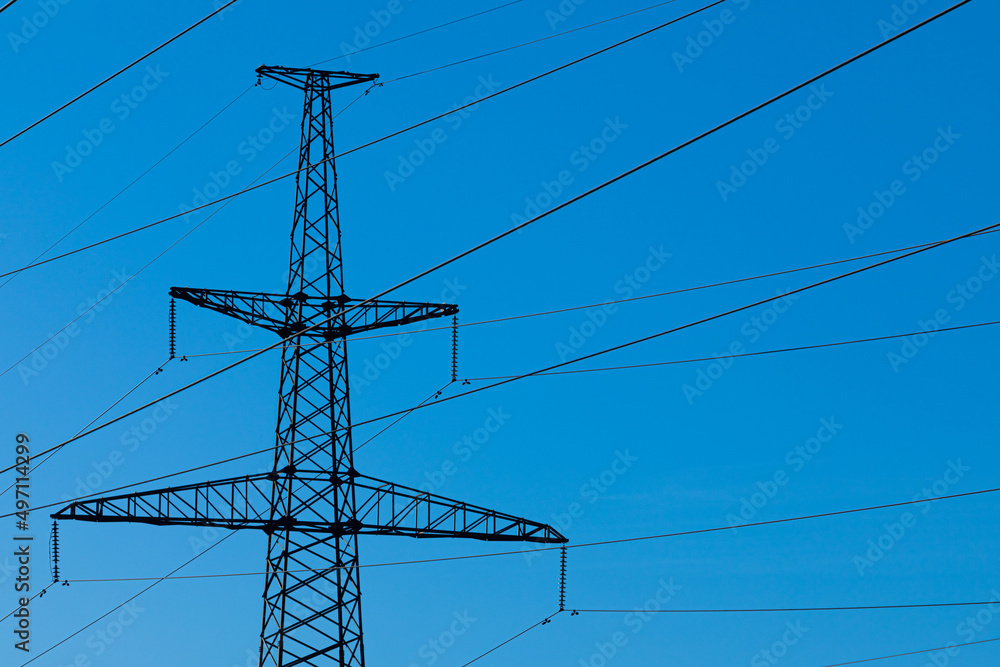 Background, view or scene of steel tower of electric main or electricity transmission line with the wires silhouette on background of clear blue sky Background, view or scene of steel tower of electric main or electricity transmission line with the wires silhouette on background of clear blue sky