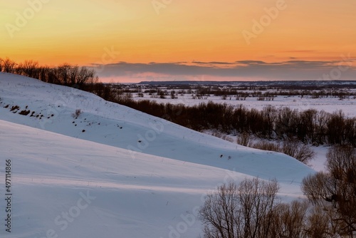 Sunset over snow-covered hills with trees on the slopes. dramatic sky
