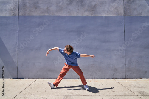 Man doing arm wave in front of gray blue wall 