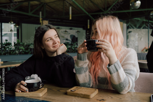 Interracial lesbian couple each other with shy smile, holding hands during lunch at restaurant.
