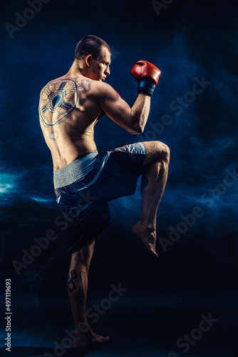 Full size of Muay thai fighter who delivering knee hit isolated on smoke background. mixed media  © zamuruev
