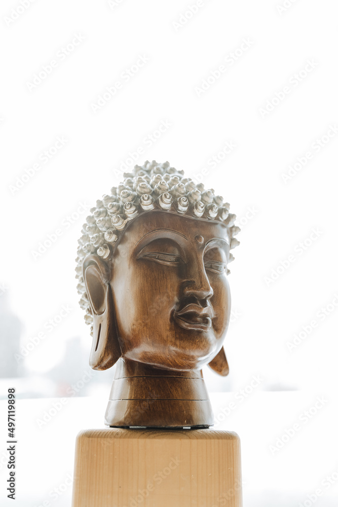 Buddha, a symbol of Buddhist culture, a statuette of the head of a Buddha, a wooden face of a god, an attribute of the interior of an apartment, an idol of Asian culture, meditation.