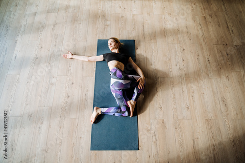 Supta Ardha Matsiendrasana, asana twisting lying on your back, stretching muscles, girl practices yoga lying on a mat, fitness in the gym, stretching photo