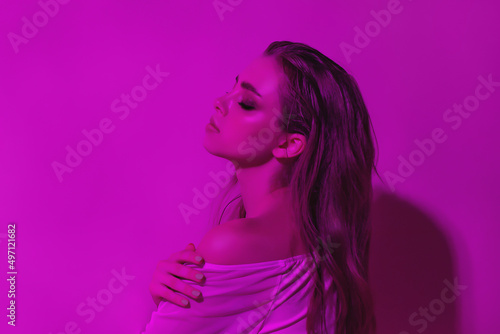 Portrait of a female fashion model in neon pink light on a dark studio background. Beautiful woman with fashionable make-up and well-groomed skin. Bright style, beauty and the concept of the future