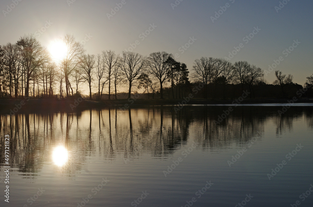 Die Morgensonne spiegelt sich zusammen mit den Bäumen im Wasser des Sees Die Morgensonne spiegelt sich zusammen mit den Bäumen im Wasser des Sees