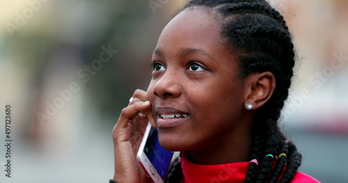 Happy black teen girl smiling and laughing talking on phone outside