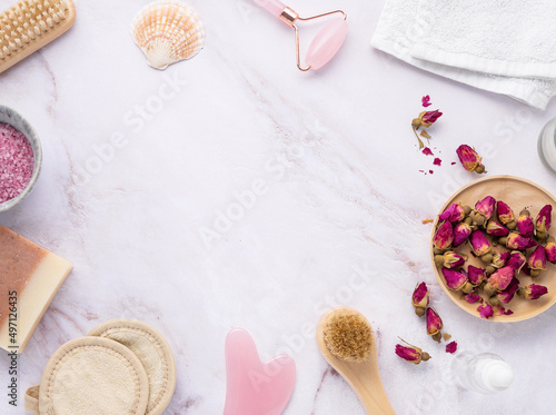 flat lay with organic sea salt with dried rose flowers, soap, candle, brush and gua sha on a pink marble background in frame. The concept of a natural spa product. Top view and copy space